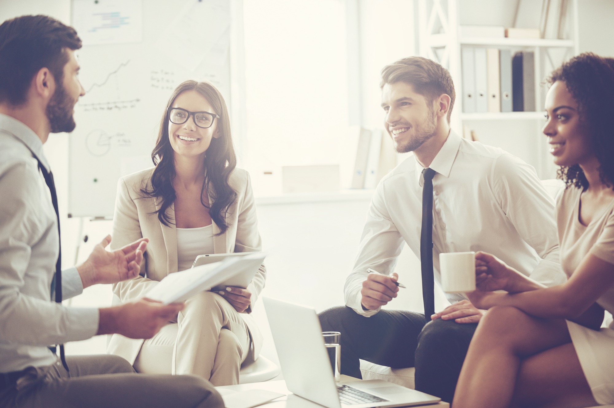 oung handsome man holding documents and discussing something with his coworkers with smile while sitting on the couch at office